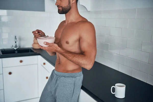 Close up of young shirtless man having breakfast while standing at home kitchen. — Stock Photo, Image