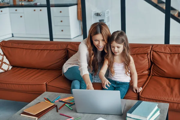 Mãe e sua filha se unindo e sorrindo ao usar laptop em casa — Fotografia de Stock