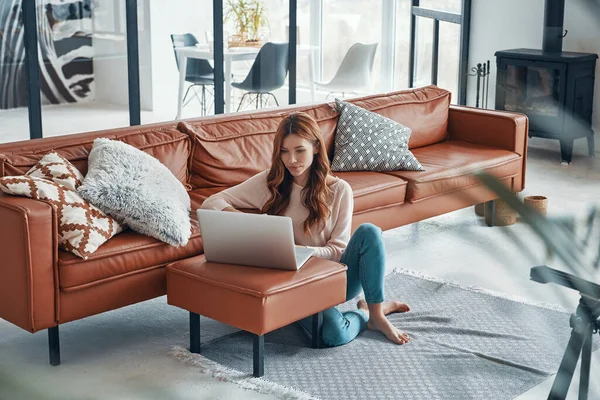 Beautiful young woman using laptop and smiling while spending time at home — Stock Photo, Image