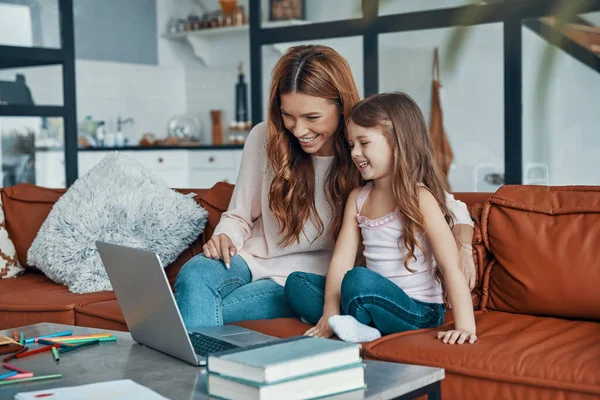 Madre y su hija se unen y sonríen mientras usan el portátil en casa —  Fotos de Stock
