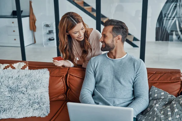 Jovem casal feliz usando laptop e sorrindo enquanto faz compras on-line em casa — Fotografia de Stock