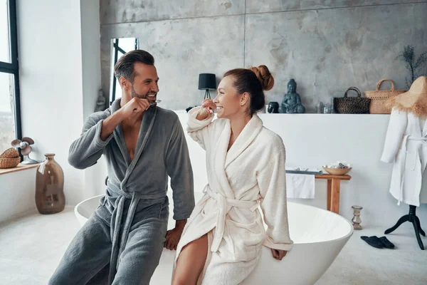 Couple in bathrobes smiling and cleaning teeth while doing morning routine — Stock Photo, Image