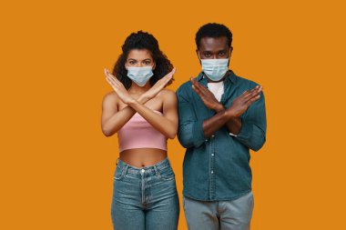 Koruyucu maskeli genç Afrikalı çift kameraya bakıyor ve el kol hareketi yapıyor.