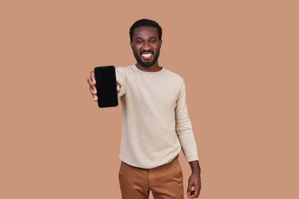 आकस्मिक कपड़े में सुंदर युवा अफ्रीकी आदमी अपने स्मार्ट फोन दिखा रहा है — स्टॉक फ़ोटो, इमेज