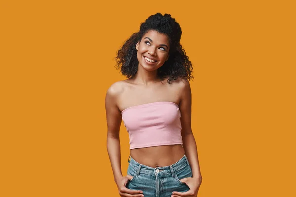 Atractivas mujeres africanas jóvenes con ropa casual manteniendo los brazos en los bolsillos y sonriendo — Foto de Stock