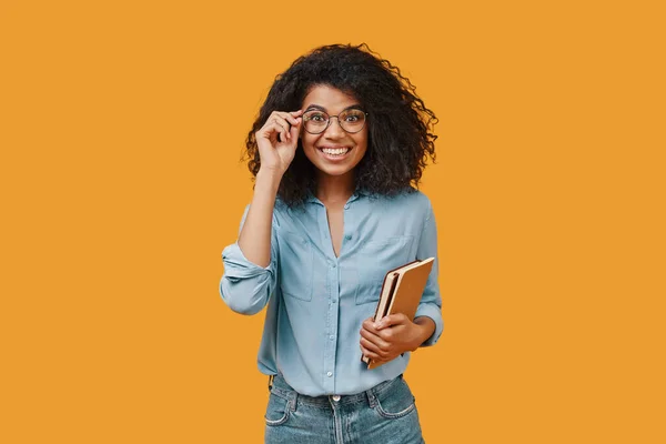 Belle jeune femme africaine en vêtements décontractés tenant des tampons de note et souriant — Photo