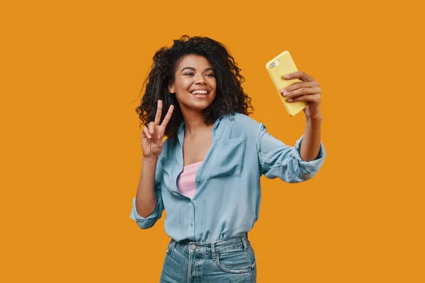 Beautiful young African woman in casual clothing taking selfie and smiling — Stock Photo, Image