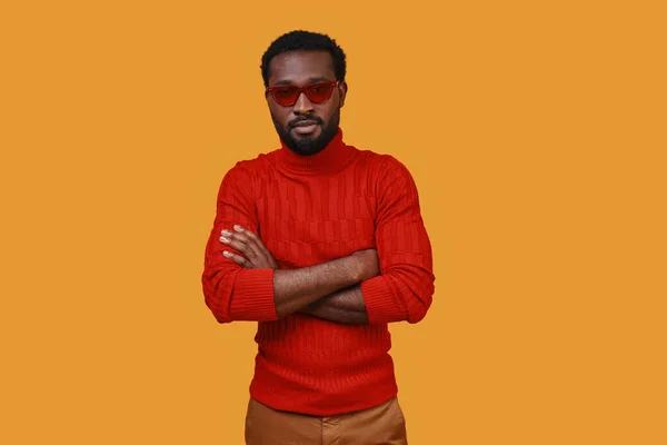 Handsome young African man in eyeglasses looking at camera while standing against yellow background — Stock Photo, Image