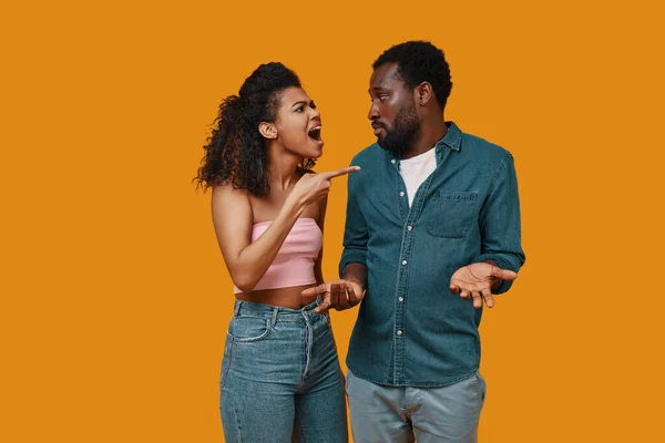 Irritada joven pareja africana gesticulando y teniendo conflicto mientras está de pie sobre el fondo amarillo — Foto de Stock