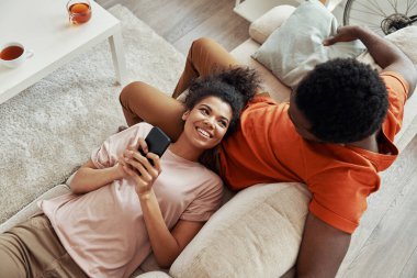 Genç Afrikalı bir kadının akıllı telefon kullanması ve evde erkek arkadaşıyla vakit geçirirken gülümsemesi.