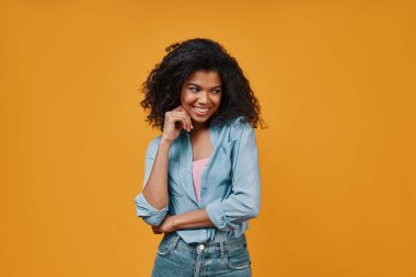 Gündelik giysiler içinde güzel bir Afrikalı kadın başka tarafa bakıyor ve gülümsüyor.