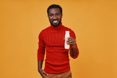 Yakışıklı genç Afrikalı adam elinde şişeyle kameraya bakıp gülümsüyor.