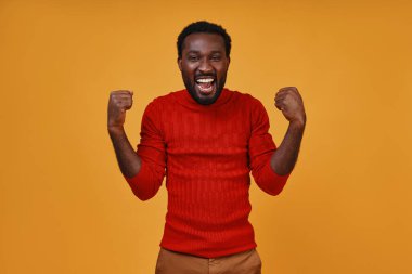 Neşeli, genç Afrikalı bir adam günlük kıyafetleriyle jest yapıyor ve kameraya bakıyor.