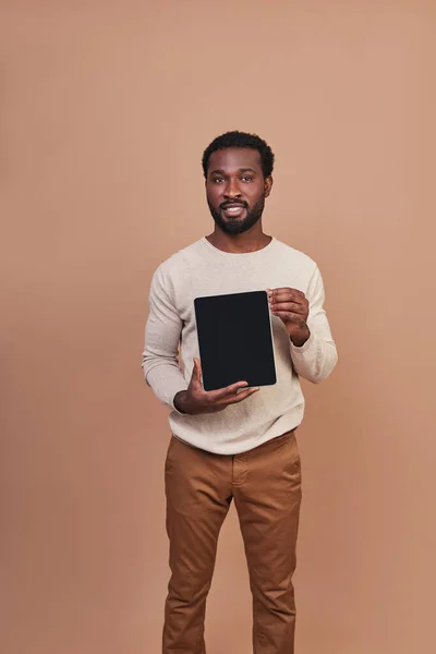 Bonito jovem africano em roupas casuais apontando espaço de cópia no tablet digital e sorrindo — Fotografia de Stock