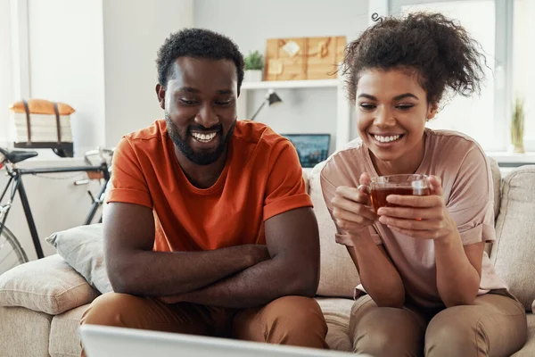 Beautiful young African couple looking at laptop and smiling while spending time at home — Stock Photo, Image