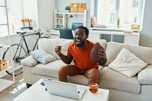 Bekymmerslös ung afrikansk man jublar och ler medan du tittar på sport match hemma — Stockfoto