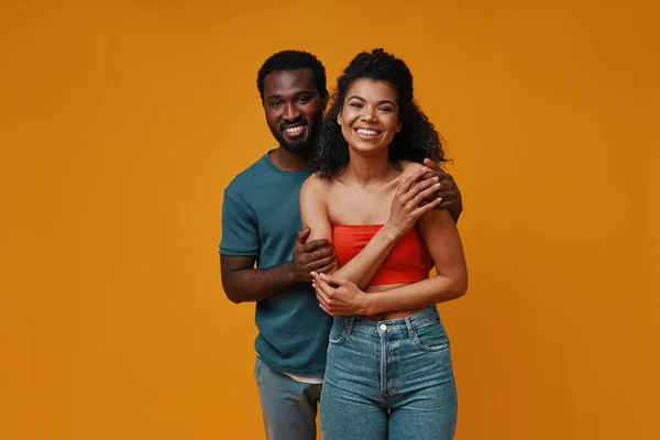 Vackra unga afrikanska par ler och omfamna när du står mot gul bakgrund — Stockfoto