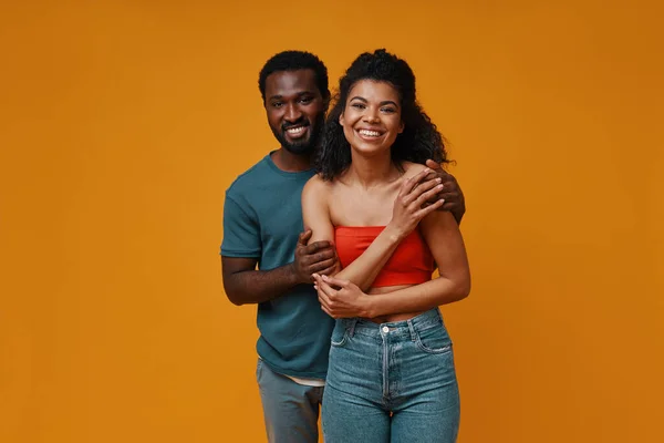 Hermosa joven pareja africana sonriendo y abrazándose mientras está de pie sobre el fondo amarillo — Foto de Stock