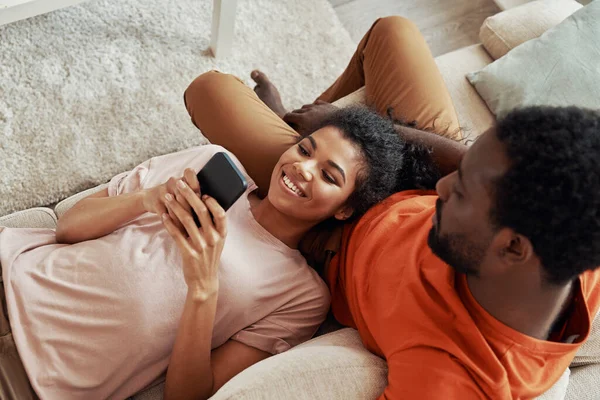 Top weergave van jonge Afrikaanse vrouw met behulp van smart phone en glimlachen terwijl het doorbrengen van tijd thuis met haar vriendje — Stockfoto