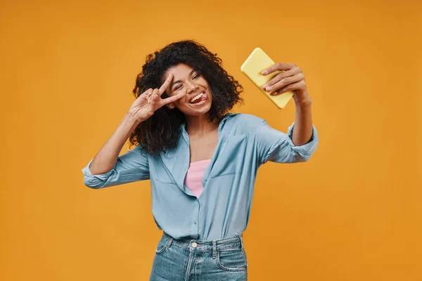 Beautiful young African woman in casual clothing taking selfie and smiling — Stock Photo, Image