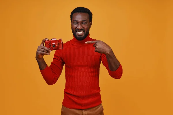 Bonito jovem africano em roupas casuais sorrindo e apontando sua câmera — Fotografia de Stock