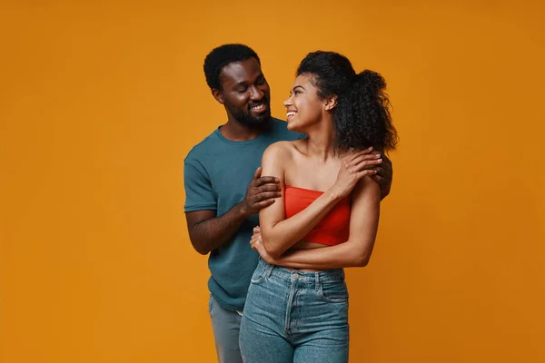 Hermosa joven pareja africana sonriendo y abrazándose mientras está de pie sobre el fondo amarillo — Foto de Stock