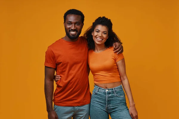 Beautiful young African couple looking at camera and smiling while standing against yellow background — Stock Photo, Image
