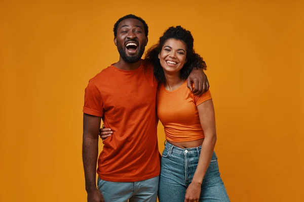 Beautiful young African couple looking at camera and smiling while standing against yellow background — Stock Photo, Image