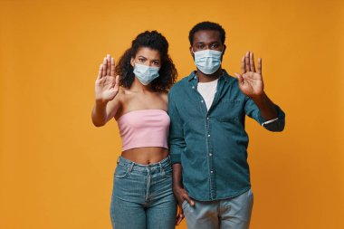 Koruyucu maskeli genç Afrikalı çift kameraya bakıyor ve el kol hareketi yapıyor.