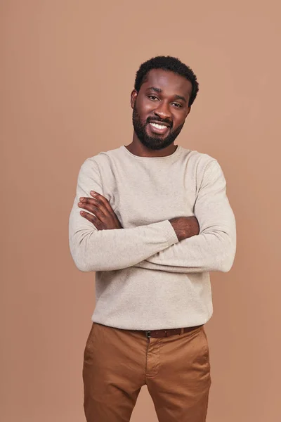 Guapo joven africano con ropa casual manteniendo los brazos cruzados y sonriendo — Foto de Stock