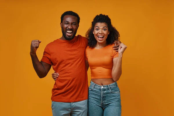 Beautiful young African couple gesturing and smiling while standing against yellow background — Stock Photo, Image