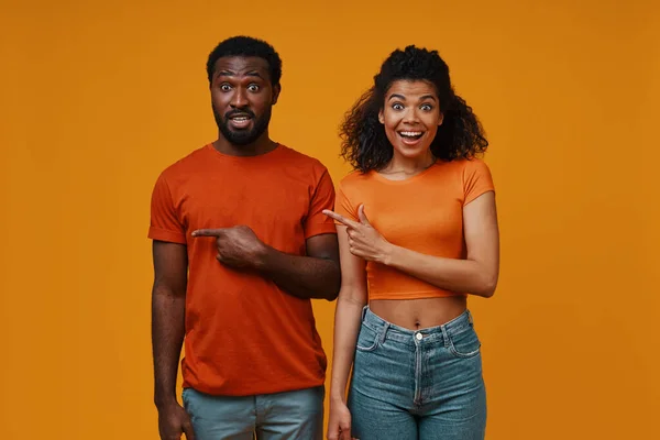 Beautiful young African couple gesturing and smiling while standing against yellow background — Stock Photo, Image