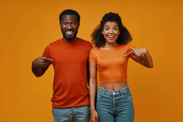 Hermosa joven pareja africana haciendo gestos y sonriendo mientras está de pie sobre el fondo amarillo — Foto de Stock