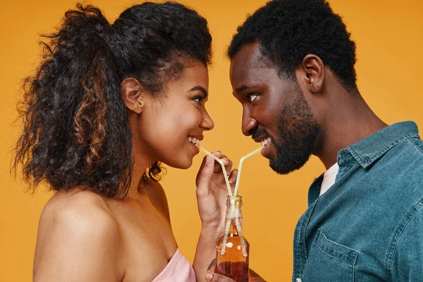 Hermosa joven pareja africana bebiendo jugo y sonriendo mientras está de pie cara a cara — Foto de Stock