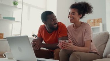 Genç Afrikalı çift dizüstü bilgisayara bakıyor ve evde vakit geçirirken gülümsüyor.