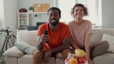 Genç Afrikalı çift evde vakit geçirirken televizyon izliyor ve gülümsüyor.