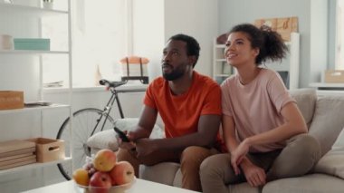 Genç Afrikalı çift evde vakit geçirirken televizyon izliyor ve gülümsüyor.