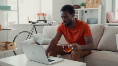Yakışıklı genç Afrikalı adam çay içiyor ve dizüstü bilgisayarla çalışıyor. 
