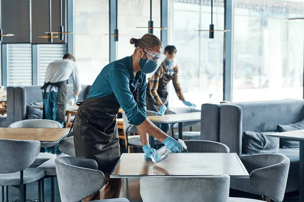 Busy young male waiters in protective workwear cleaning tables in restaurant — 스톡 사진