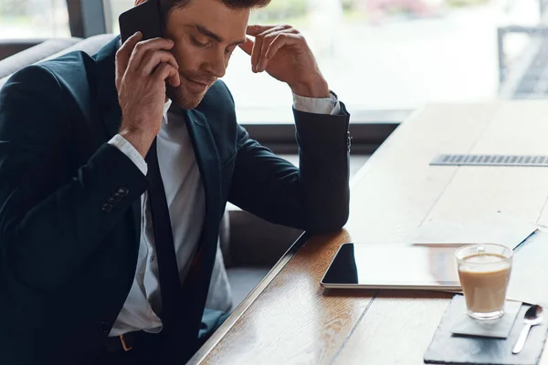 Thoughtful young businessman in full suit talking on the smart phone while sitting in the restaurant — Stock fotografie