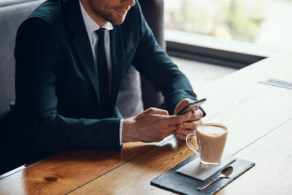 Close up of young businessman in full suit using smart phone while sitting in the restaurant — Stock Photo, Image