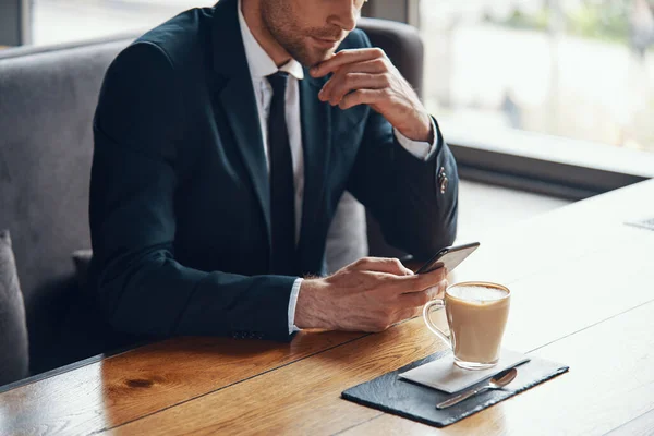 Close up of young businessman in full suit using smart phone while sitting in the restaurant — Stock Photo, Image