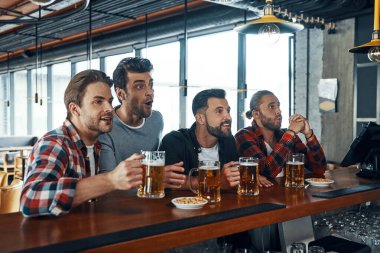 Sıradan giysiler içinde genç erkeklere tezahürat yapmak bira içmek ve barda otururken maç izlemek.