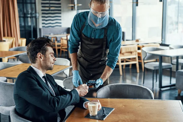 Stilig ung affärsman gör en kontaktlös betalning medan du sitter i restaurangen — Stockfoto