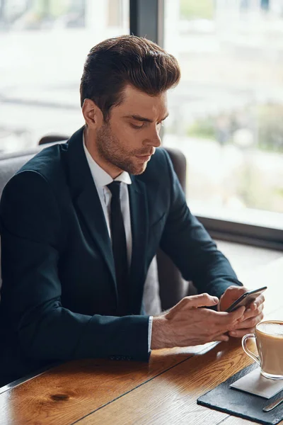 Handsome young businessman in full suit using smart phone while sitting in the restaurant — Stock fotografie