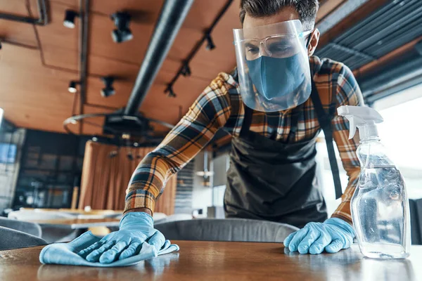 Busy man in protective face shield cleaning table in restaurant — 스톡 사진