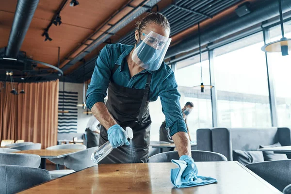 Unga manliga servitörer i skyddsarbetskläder rengöringsbord i restaurang — Stockfoto