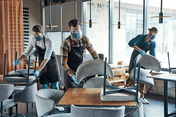 Young male waiters in protective workwear arranging furniture in restaurant — Stock Photo, Image