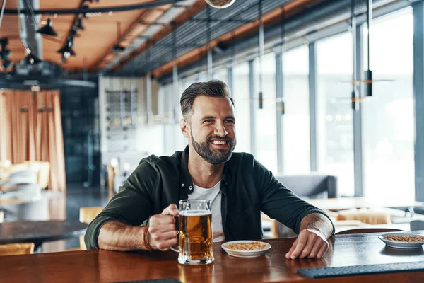 Happy young man in casual clothing drinking beer while spending time in the pub — 图库照片