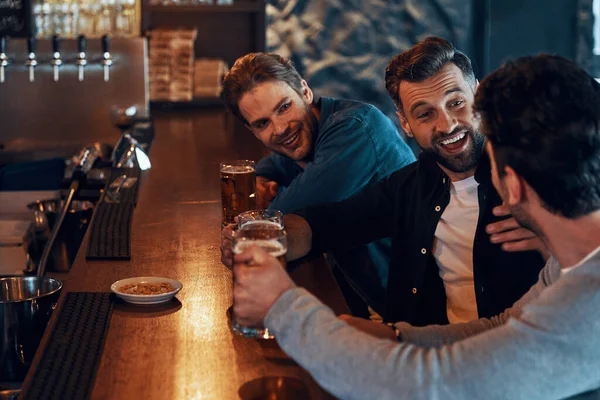 Unbekümmerte junge Männer in lässiger Kleidung, die Bier trinken und in der Kneipe zusammensitzen — Stockfoto